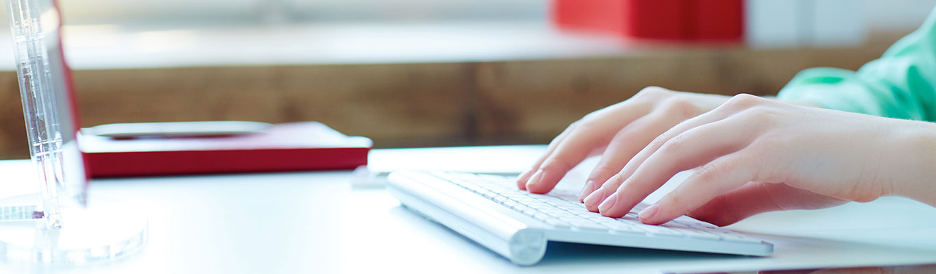 Woman's hands typing on a keyboard in front of a computer screen.