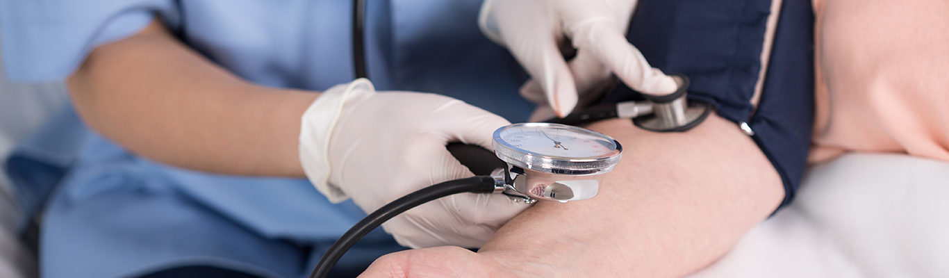 Nurse or doctor wearing gloves with a stethoscope measuring blood pressure on a patient.