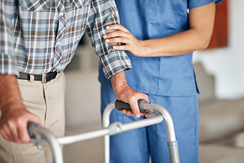 Home health nurse assisting man with mobility aid.