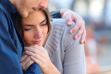Man comforting woman with his arms on her shoulder