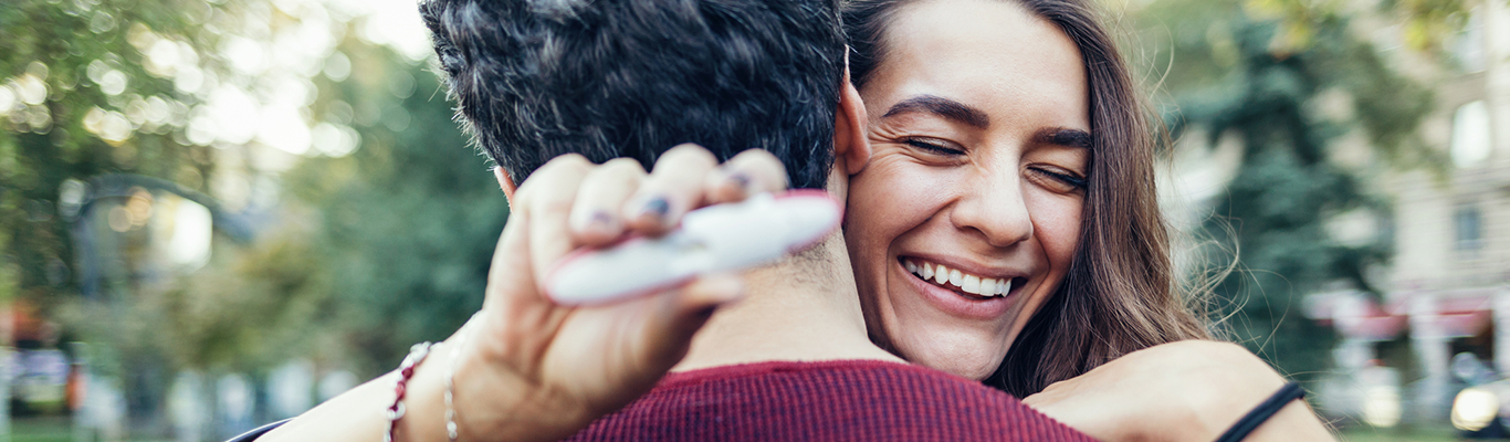 Women holding pregnancy test while hugging male