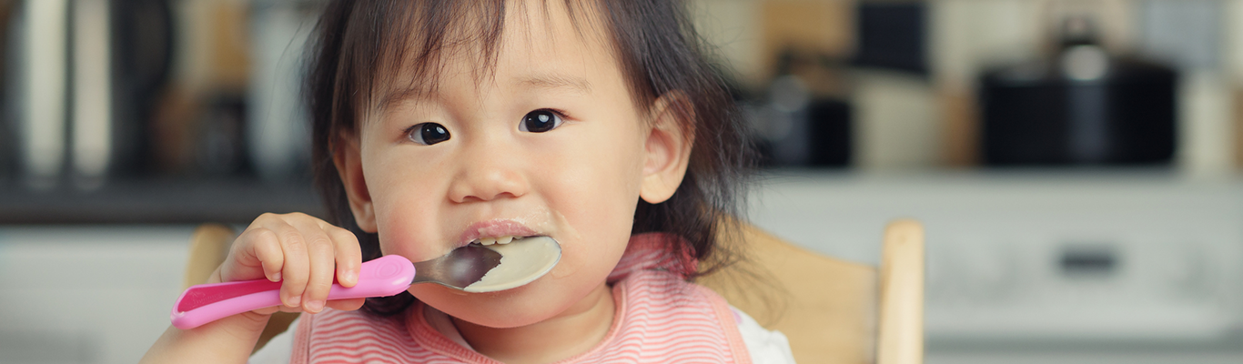 Asian girl spoon feeding at the table