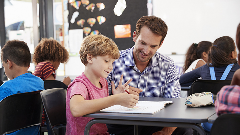 Young male teacher with student at desk