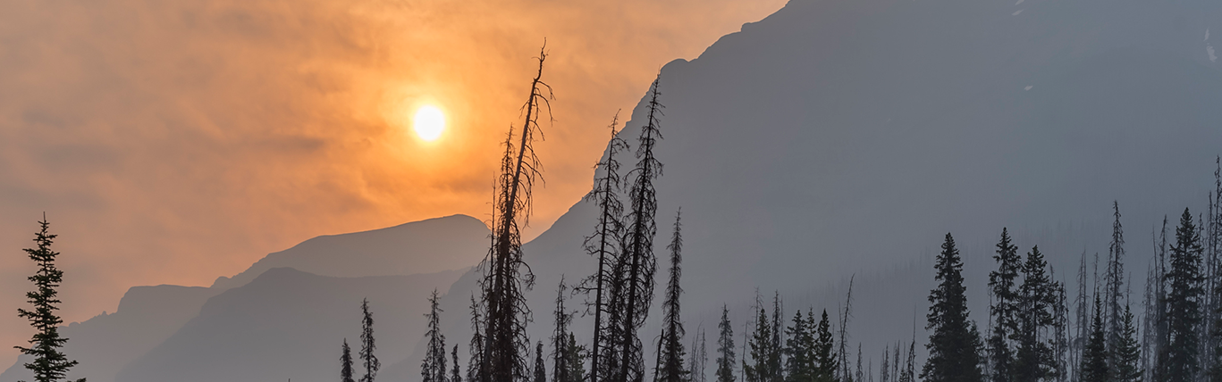 Sun through orange hazy skies over a forested mountain
