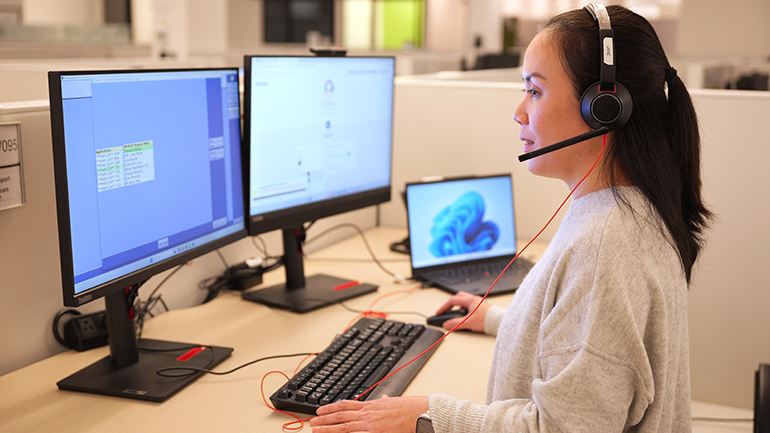 Registered nurse wearing a headset sitting at a desk in front of computer screens