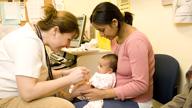 Child sitting on mother's lap while nurse is smiling at the child