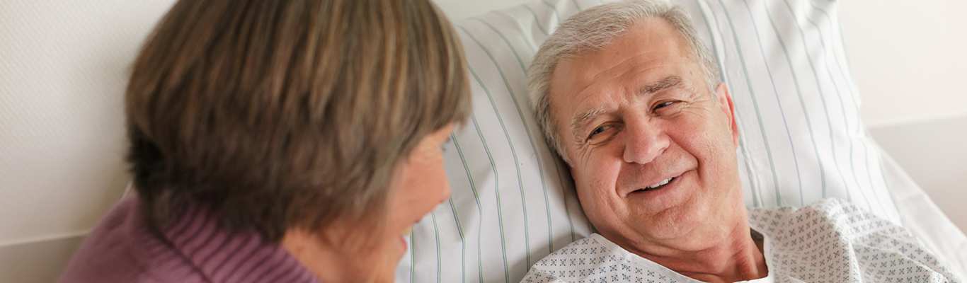 Senior male patient in bed with female family member.