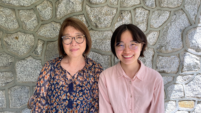 Two people posing for photo in front of stone wall.