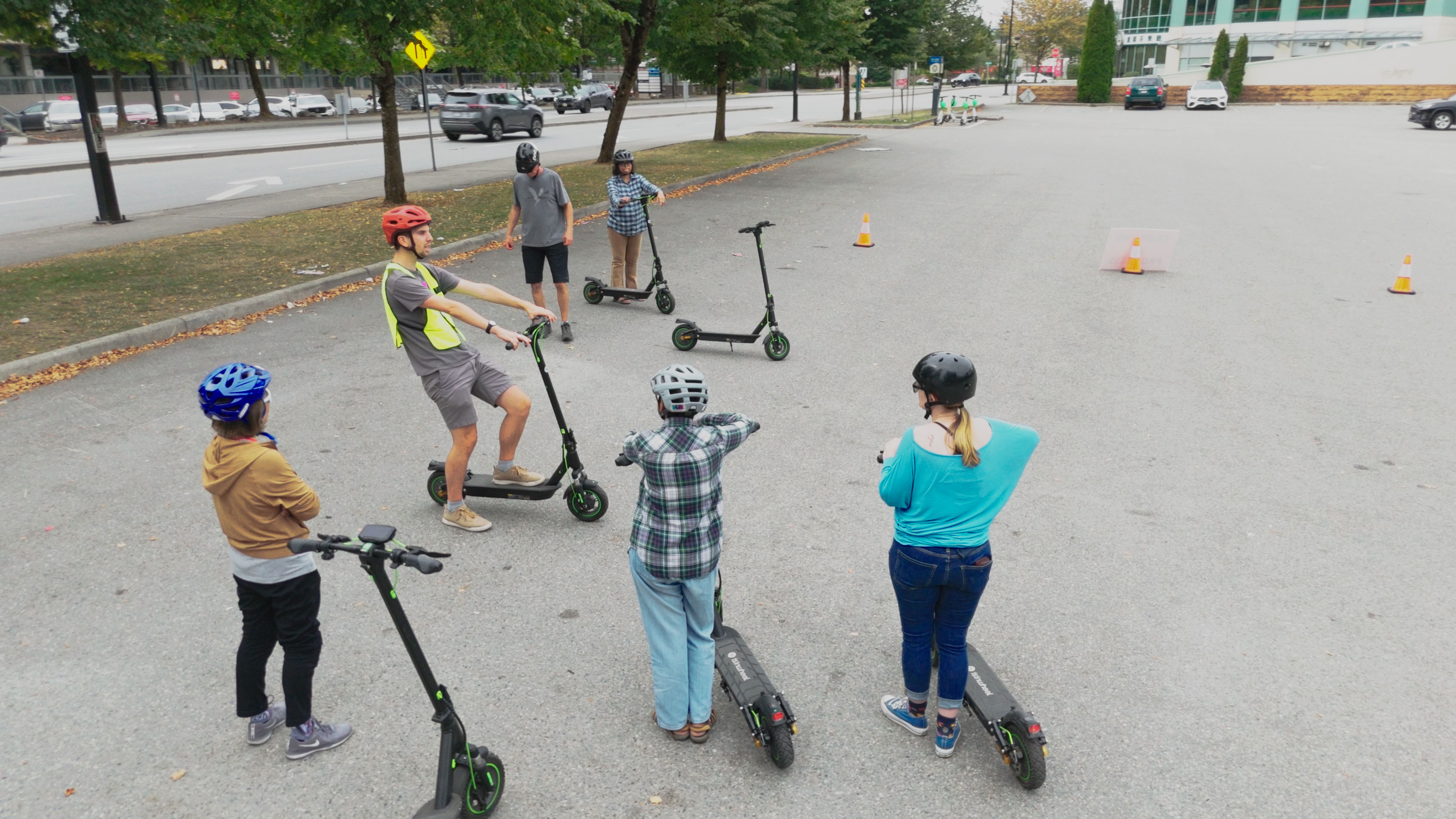 A group of teens with e-scooters gather around an instructor for an e-scooter lesson in a parking lot