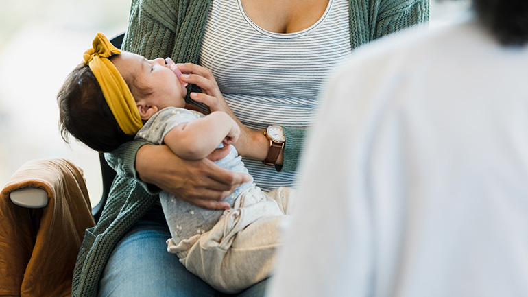 Baby looks up at a person putting a pacifier in their mouth.