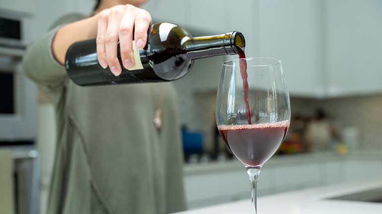 Women pouring red wine into a wine glass in her kitchen.