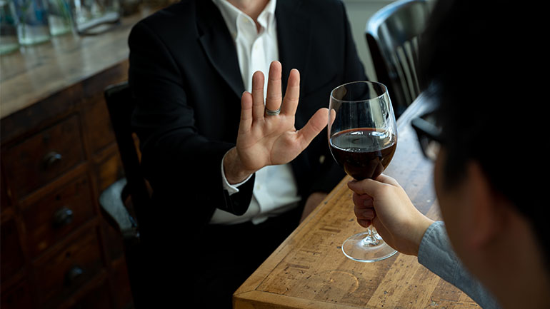 a man refusing red wine being offered to him