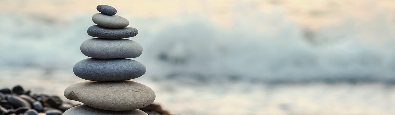 Stones piled up largest to smallest on the left side of the image on a rocky surface by the water