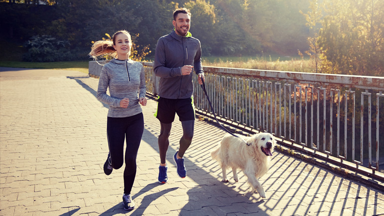 A young woman and man jogging on a bridge with their dog