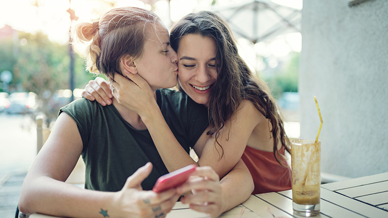 Young happy women drinking ice coffee outdoors on a hot summer day, embracing, kissing and having fun
