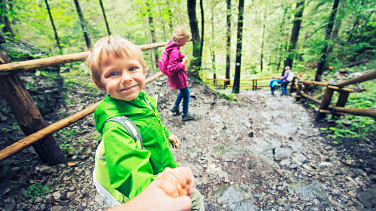 child in green jacket holding onto hand of adult while hiking