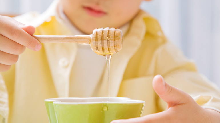 Child holding honey dipper above a bowl of honey