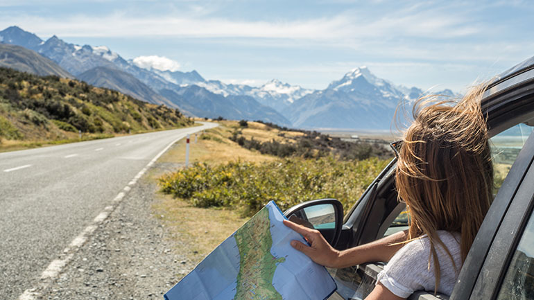 woman sitting in her car on the side of the road with a map in her hand looking at the mountain skyline