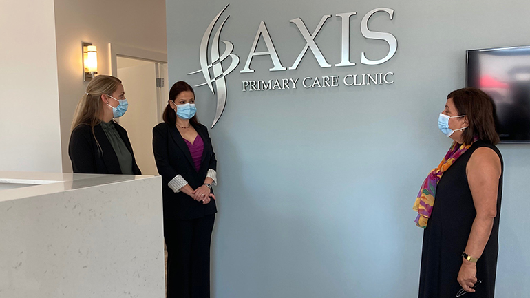 Panorama MLA Jinny Sims, Lexi Grisdale, the clinical director and Tatiana Radosavljevic, nurse practitioner, with the Axis Primary Care Clinic. They are standing by the front desk under the Axis Primary Care Clinic sign.