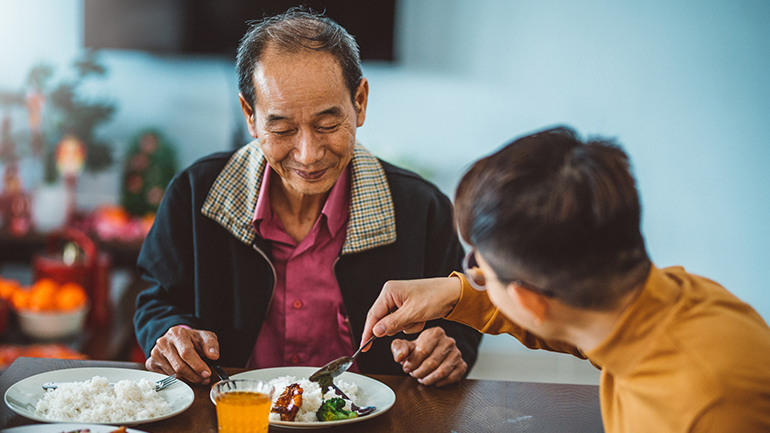 An Asian man sharing food to his father while enjoying reunion dinner at home during Chinese New Year