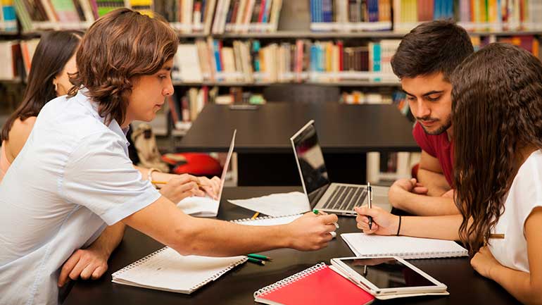 Students studying and teaching each other at a library