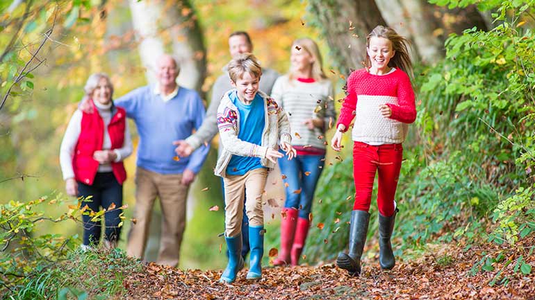 Family walking with kids running and playing with the fallen leaves
