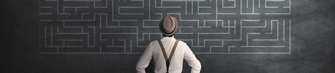 Man in hat looking at an image of a maze on a chalkboard.