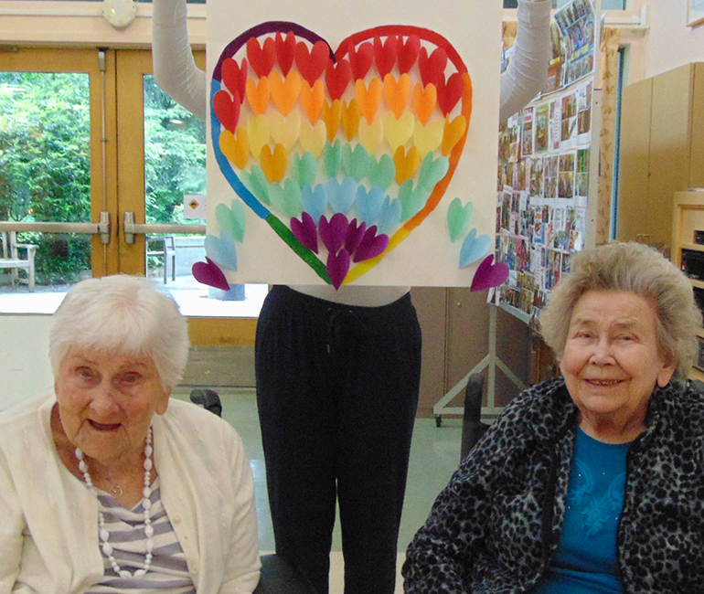 Rainbow heart artwork and two seated people smiling