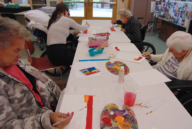 Four people sitting at a table painting